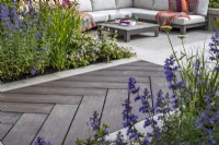 A boardwalk leading to the patio made of wood imitation material and surrounded by a perennial bed planted with Nepeta. June. Designer: Kevin Dennis 