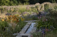 Rill in late summer walled garden, informal planting of drought tolerant plants in gravel