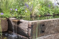 Water falling from a rill in ponds made from reclaimed sleepers. Backdrop of plants including grasses and Geranium 'Rozanne' - Caroline and Peter Clayton - Get Started Gardens - Nurturing Nature in the City, RHS Hampton Court Palace Garden Festival.