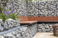 A seating area using reclaimed wood against a boundary wall made of gabions filled with stone offcuts - - Caroline and Peter Clayton - Get Started Gardens - Nurturing Nature in the City, RHS Hampton Court Palace Garden Festival.