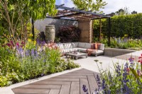 Contemporary garden with secluded seating area, steel pergola, walking board and large ceramic pot. Flower beds planted with Acer palmatum, Heptacodium and coloured perennials. June, Designer: Kevin Dennis, Bord Bia Bloom 2023