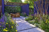 Garden space surrounded by a navy blue painted panels with path with an original leaves design and relaxation area with decorative wooden deckchairs set against living green wall under openwork of pergola roof. Planting includes: Achillea millefolium 'Moonshine', Nepeta faassenii 'Junior Walker, Salvias nemorosa 'Caradonna Pink', 'Amethyst' and  multi-stem Lagerstroemia indica. June
Bord Bia Bloom, Dublin
Designer: Jane McCorkell
