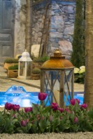 Decorative lantern and purple tulips nex to a small pond with floating candles in contemporary Italian courtyard.