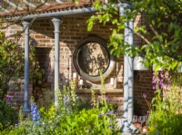 Circular mirror on brick wall  in an outdoor dining room. The Savills Garden, Designer: Mark Gregory, RHS Chelsea Flower Show 2023, May, Spring, Summer