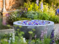 Water bowl feature with floating flowers of Delphinium. The Savills Garden, Designer: Mark Gregory, RHS Chelsea Flower Show 2023, May, Spring, Summer