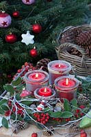 Advent wreath with candles in jars on a tray, decorated with moss, holly branches and cones 
