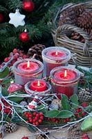 Advent wreath with candles in mason jars on a tray, decorated with moss, holly branches and cones 
