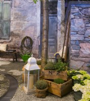 Display of herbs and Hydrangea in containers and lantern in front of the stone house of contemporary Italian courtyard. A water canal running on the gravel surface. 