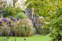 View across the lawn to ruins and Autumn border with mixed grasses including Miscanthus sinensis 'Sirene' and Matteuccia struthiopteris.