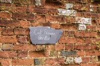 Slate sign hanging on a brick wall at Cerney House Gardens in March