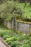Stone wall with entrance way framed by gate posts topped with pineapple finials at Cerney House Gardens in March