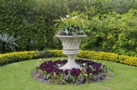 Lattice weave urn with an arrangement of white tulips and variegated cordyline underplanted with decorative foliage standing in the middle of a circular island flowerbed, Avenue Gardens, The Regent's Park, London, UK 