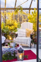 Recycled plastic chairs with blankets and cushions in greehouse decorated with mixed plants and fairy lights