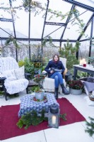 Woman reading magazine in large greenhouse decorated with fairy lights and mixed plants