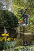 View across water at Keukenhof Gardens, The Netherlands, in spring.  A miniature windmill behind and a 'clog' boat in the spring garden