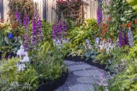 Summer bed along stone and gravel path planted with Digitalis purpurea, ferns, Lupinus and Geum. Designer: Darragh Collopy, Bord Bia Bloom 2023 