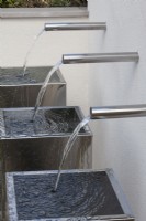 Three chrome water spouts cascading into metal containers in the 'Sociability' garden at BBC Gardener's World Live 2015, June