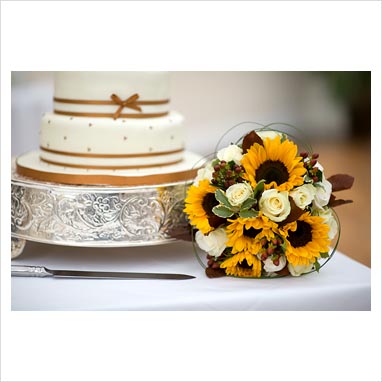 wedding bouquet of white roses and sunflower alongside a wedding cake