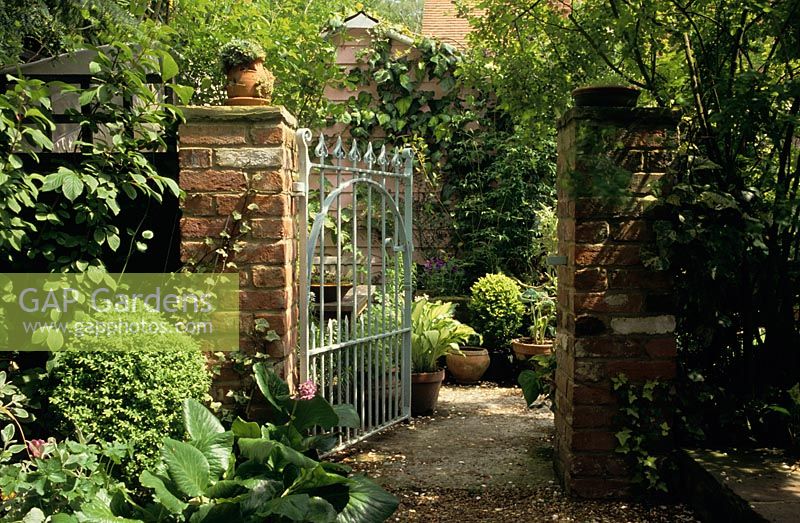 Cast iron gate in brick wall with view to small garden at Lime Tree Cottage in Surrey