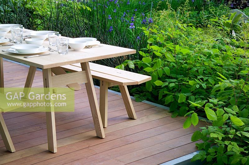 Decking with dining table surrounded by lush green planting at The Laurent Perrier'Harpers Queen Garden at Chelsea FS 2004