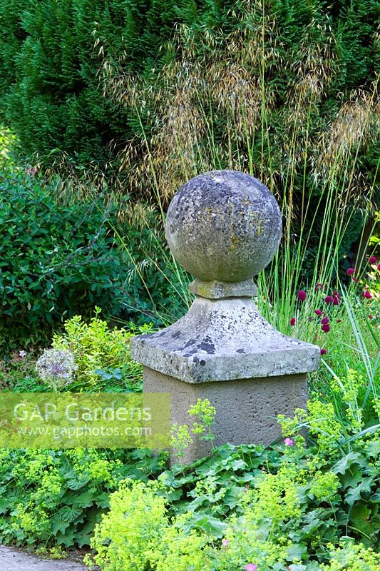 Stone sphere in informal border with Alchemilla mollis and Stipa at Lower House, Powys in Wales