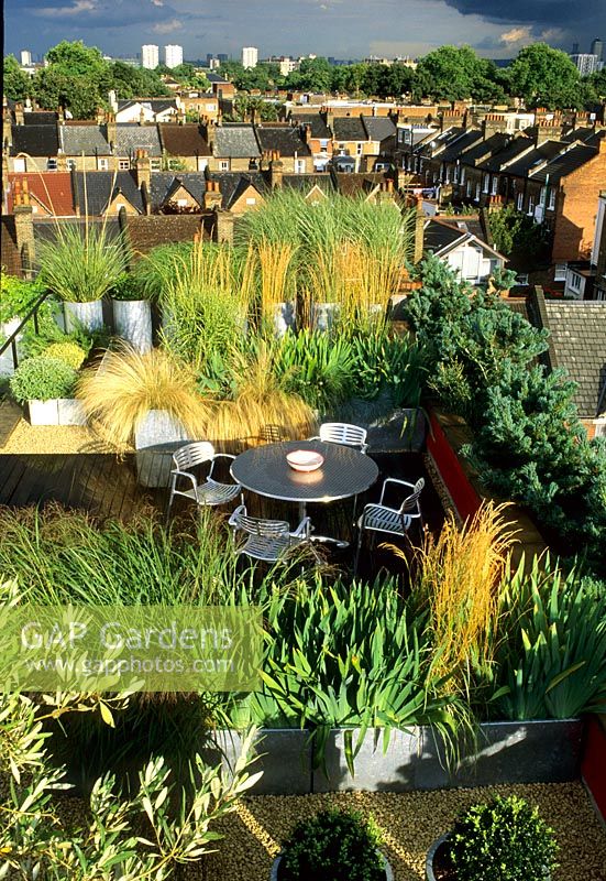 Roof garden with decking, metal furniture and square metal containers planted with grasses