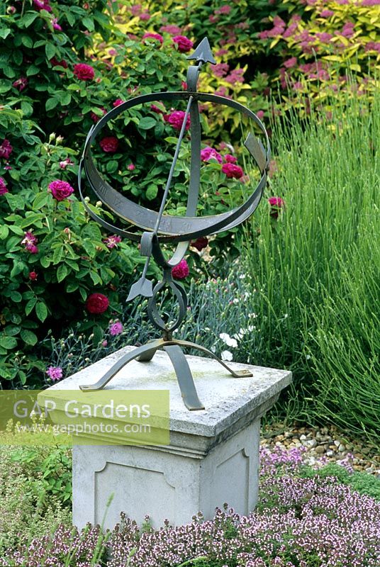 Sundial in garden on stone plinth with Thymus and Roses