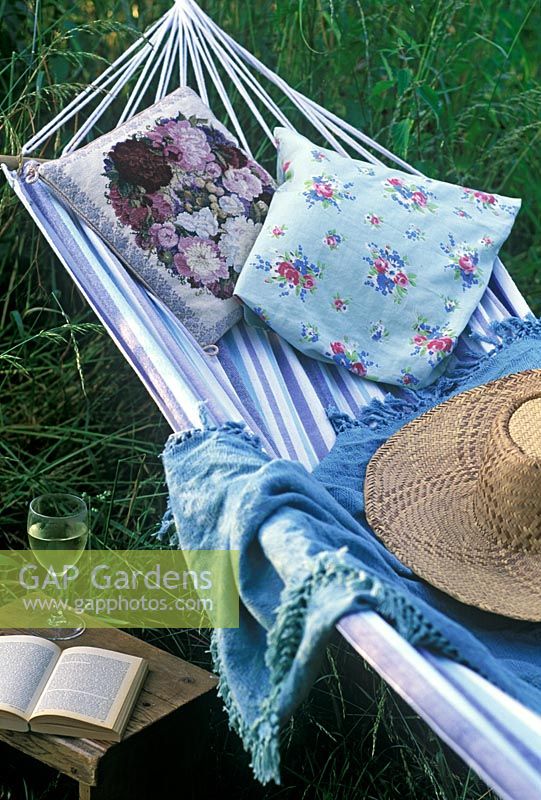 Striped Hammock with cushions, hat and shawl and glass of white wine with open book on small wooden table at Rose Cottage