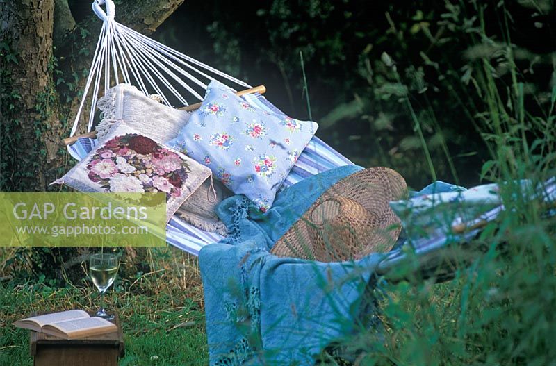 Striped Hammock with cushions, hat and shawl and glass of white wine with open book on small wooden table at Rose Cottage.