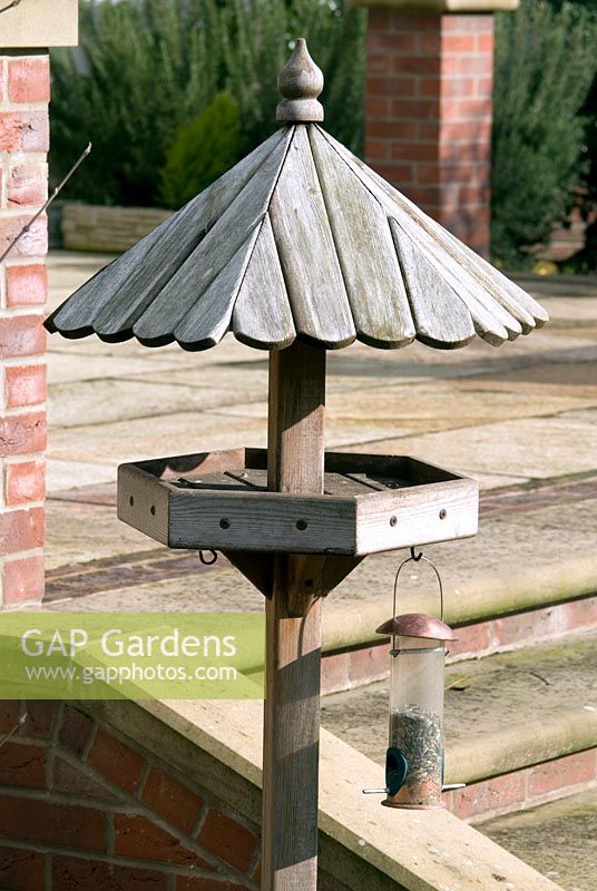 Wooden bird table and bird feeder with sunflower seeds hanging from a hook
