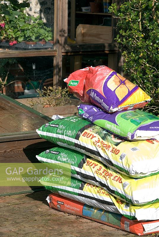 Bags of multi purpose compost, mini bark chippings, lawn dressing and bulb compost  by the green house and cold frame