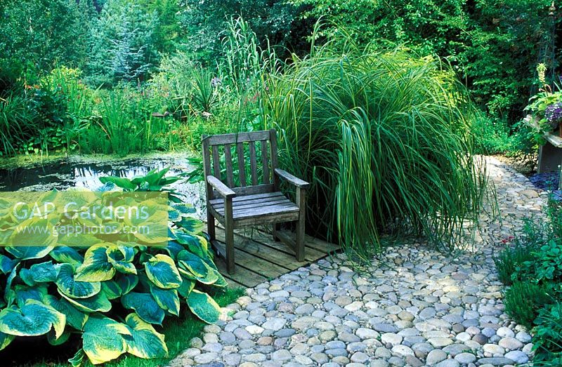 Winding cobble path by Garden pond with grasses and Hostas at Barleywood