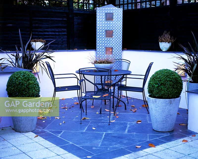 Urban courtyard terrace with furniture, paving, containers and lighting in dusk