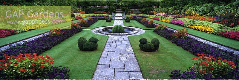 Multi-coloured annual bedding, fountain & topiary. Hampton Court Palace, Surrey, England, UK.
