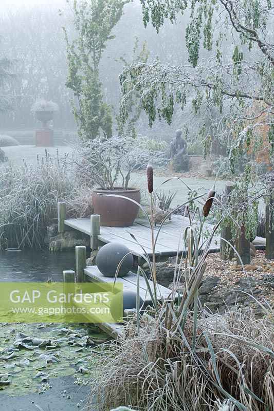 A foggy, frosty morning by the frozen pond in John Massey's garden. Statue, urn and container all acting as focal points. Deck with bronze balls. Bullrushes in the foreground.