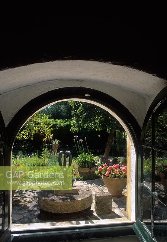View through open window to Mediterranean style garden beyond with containers and ornament on patio - Corfu