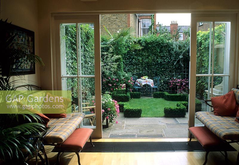 Contemporary interior of house looking out through double doors in to small garden with laid table in background - Fulham
