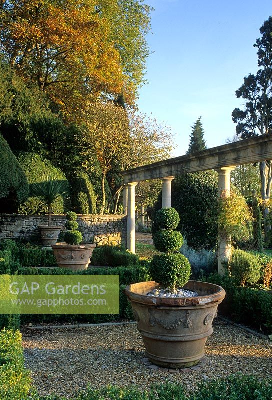 Italianate formal garden with gravel paths, low Buxus hedging, topiarised Buxus in terracotta containers and tall columns - 
Iford Manor