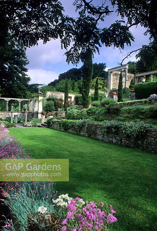 Italiante terraced formal garden with retaining walls, steps, tall Cupressus, columns and containers - Iford Manor