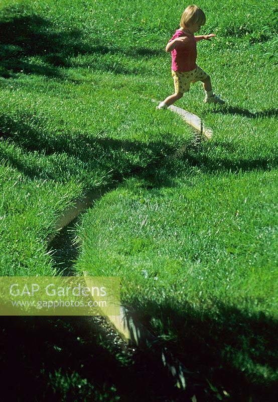 Child hopping across rill in lawn - The Healing Garden MA, USA