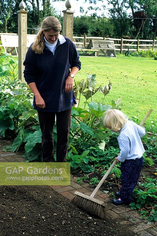 Woman and child sweeping path in vegetable garden - Pannells Ash Farm, Essex