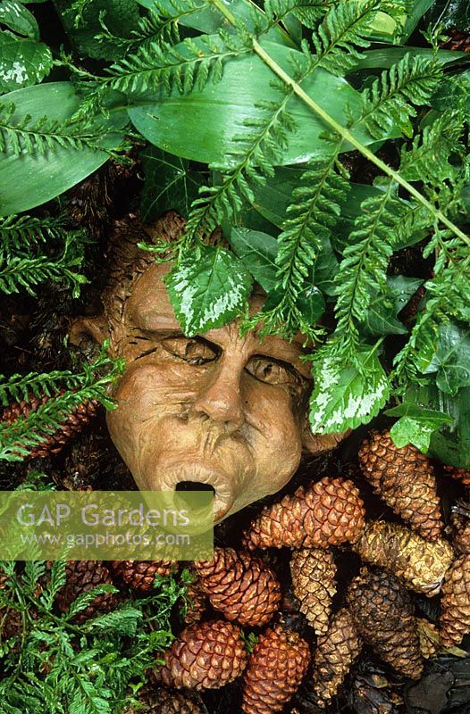 Mask sculpture placed amongst ferns and fir cones