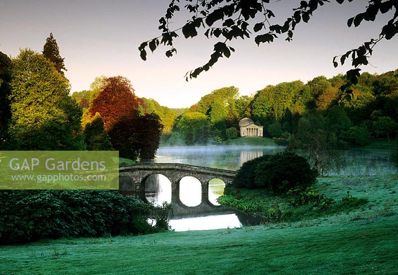 Early morning mist and bridge over lake - The Temple Pavilion on the far side reflected in the water - Stourhead, Stourton, Wilts