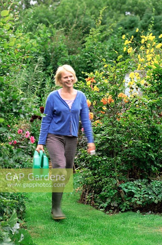 Woman walking through garden with watering can