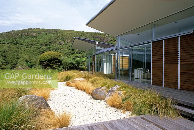 Garden view with boulders and native grasses contrasting with modern building in Piha, New Zealand. Garden Design - Ted Smyth. 