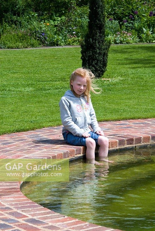 Girl with feet in the water of a Natural Swimming Pond on the edge of the Wimpole Hall Estate, Cambridgeshire