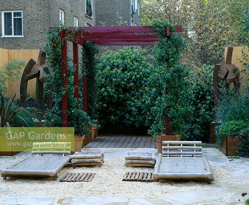 Roof garden with barleycorn gravel, bamboo chairs, red pergola and rusted steel sculpture