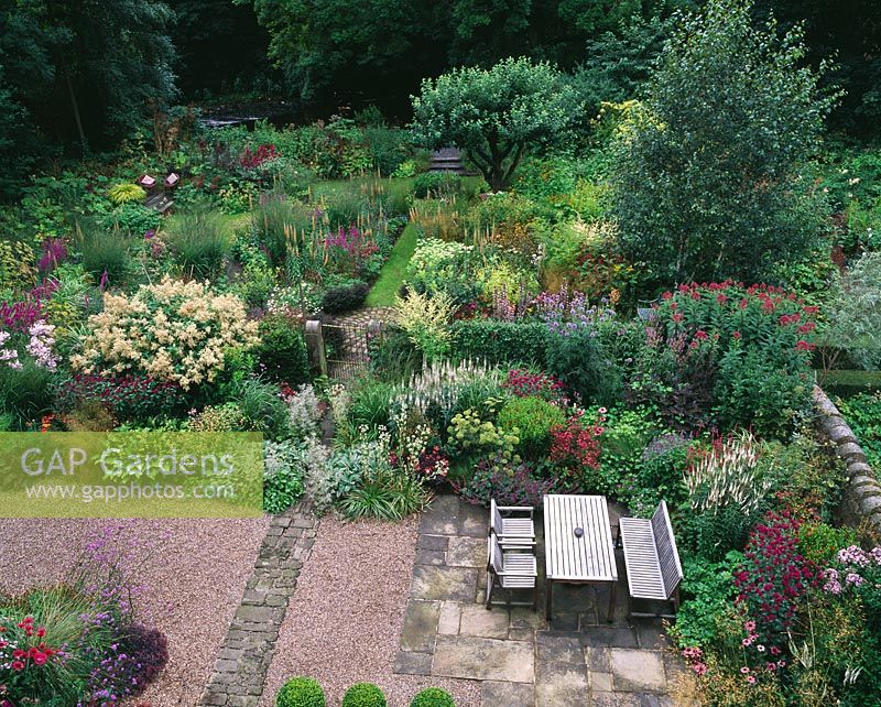 View from above of herbaceous perennial borders and seating area with table and chairs at Mayroyd Mill House, Yorkshire. Design Richard Easton and Steve Mackay.