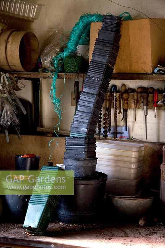 Black plastic plant pots stacking in a potting shed with old tools and garden twine