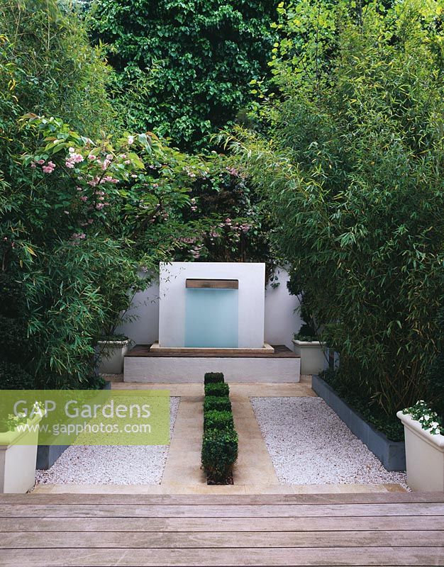 Modern minimalist garden with gravel parterre, Buxus - Box squares at centre, leading to simple water feature. Charles Worthington's garden designed by Stephen Woodhams